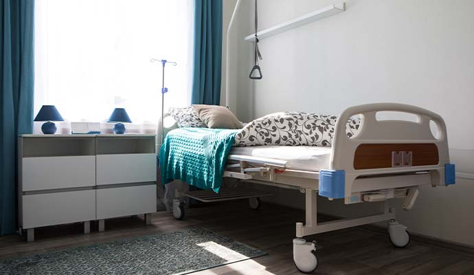 A clinical patient room featuring an empty adjustable medical bed