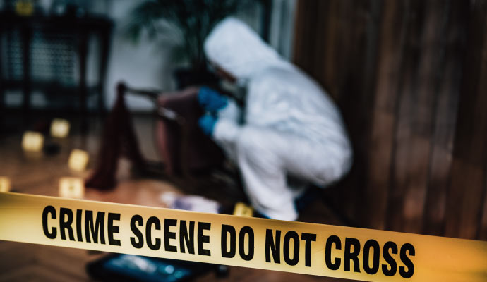 Investigator cleaning a crime scene area secured with yellow tape
