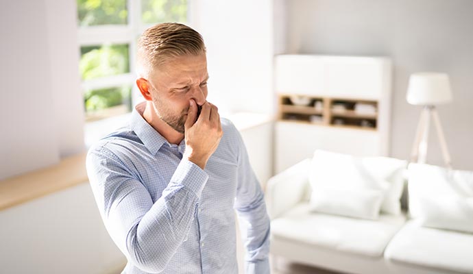 A man holding his nose and reacting to a bad smell in a modern living room